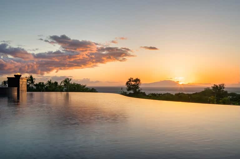 Infinity pool overlooking ocean at golden sunset with palm trees and architectural elements