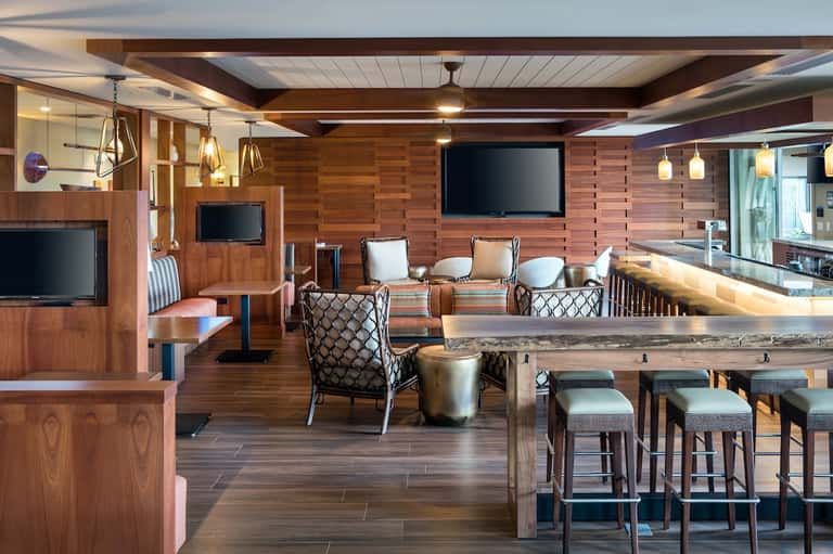 Wooden interior of luxury lounge or clubhouse with bar, seating areas, multiple TV screens, and pendant lighting