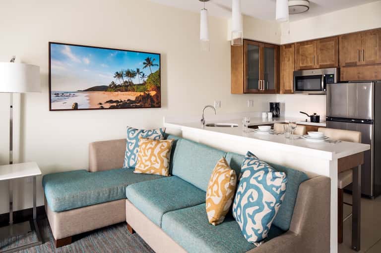 Bright hotel suite living area with coastal artwork, turquoise accents, and kitchen