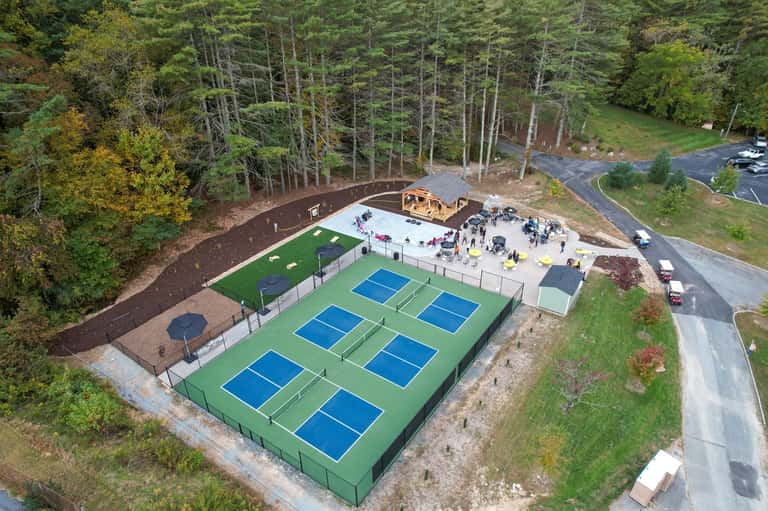 Aerial view of pickleball courts with green playing surfaces surrounded by forest