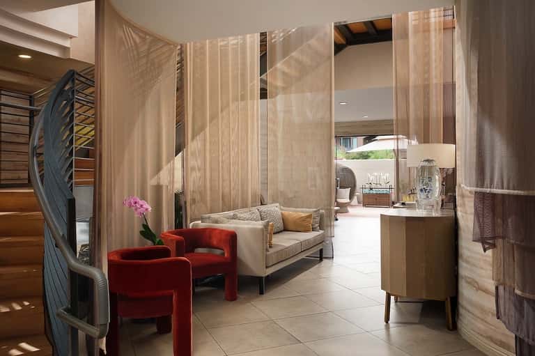 Luxury spa suite with sheer curtains, red accent chairs, beige sofa, wooden furnishings, and terraces