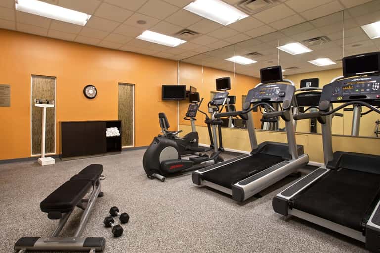 Fitness center with orange walls, treadmills, exercise bikes, dumbbells, and cardio equipment