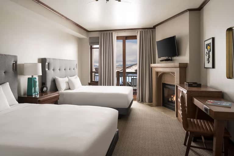 Upscale hotel room with two queen beds, fireplace, balcony with scenic mountain views, neutral decor