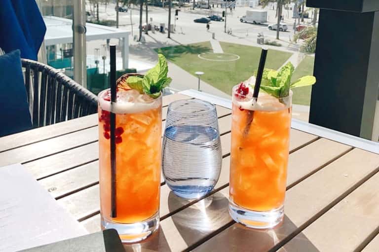 Two colorful cocktails with mint garnish on a high-rise balcony overlooking a golf course