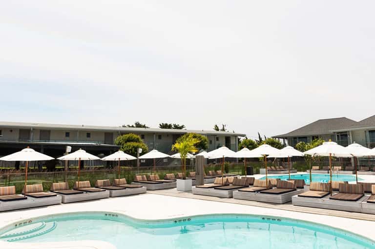 Resort pool deck with white umbrellas, striped lounge chairs, and calm turquoise water