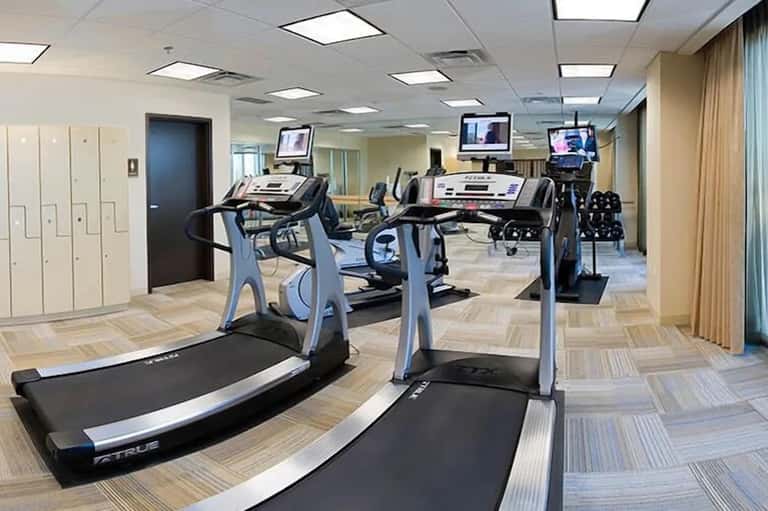 Compact hotel fitness room with treadmills, exercise bikes, and overhead lighting