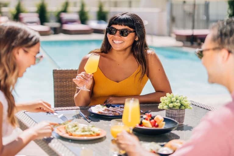 Three women dining poolside with fresh food, beverages, and pool in background