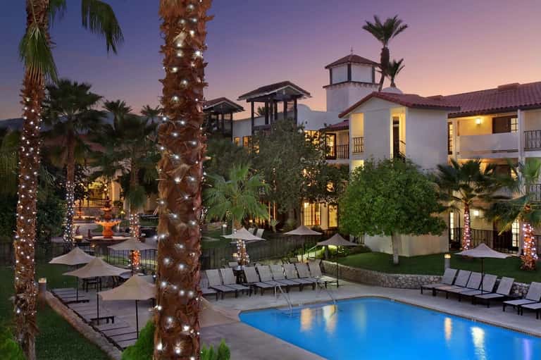 Luxury resort courtyard at dusk with illuminated palms, pool, and architecture