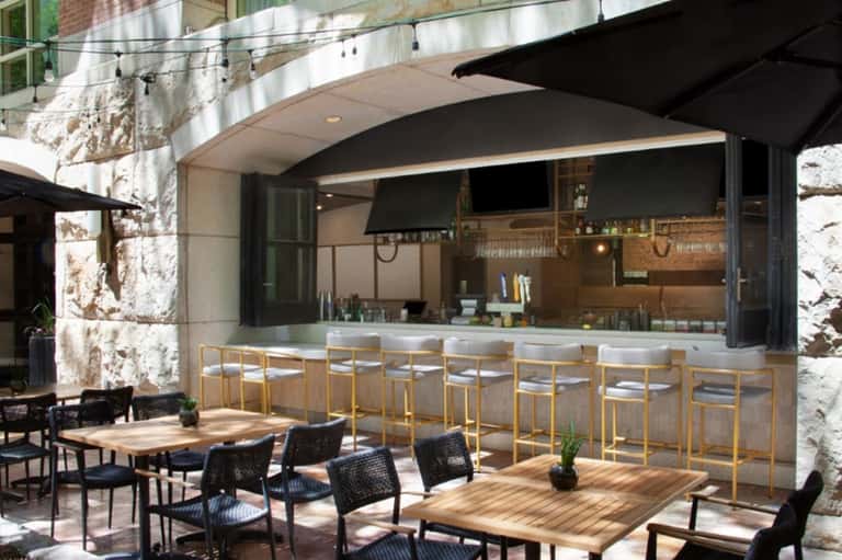 Modern outdoor bar and dining patio with wooden counter, bar seating, and stone architectural elements