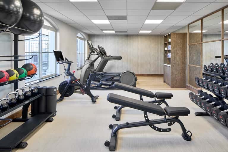 Fitness gym with exercise equipment, dumbbells, stationary bike, natural light, and modern interior design