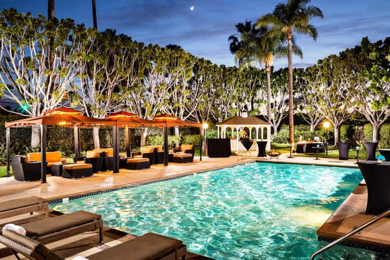 Twilight poolside lounge with orange umbrellas, palm trees, and comfortable seating