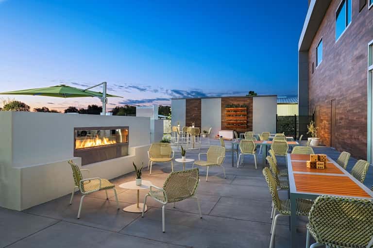 Modern rooftop patio at dusk with fireplace, dining tables, and shade structures against twilight sky