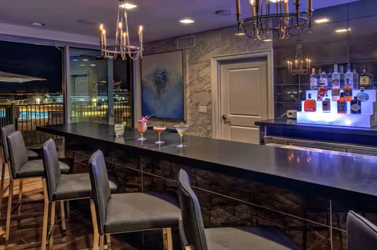 Luxury penthouse bar with dark countertop, lit bottle display, and city views