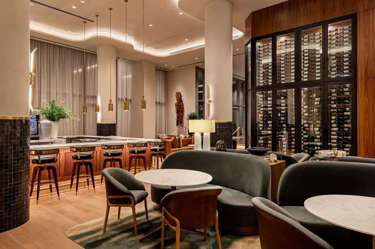 Contemporary wine lounge with curved seating, marble tables, floor-to-ceiling wine display, and pendant lights