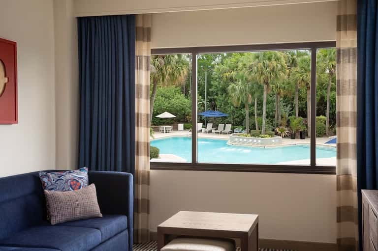 Hotel room interior with blue sofa overlooking large windows framing the resort pool area
