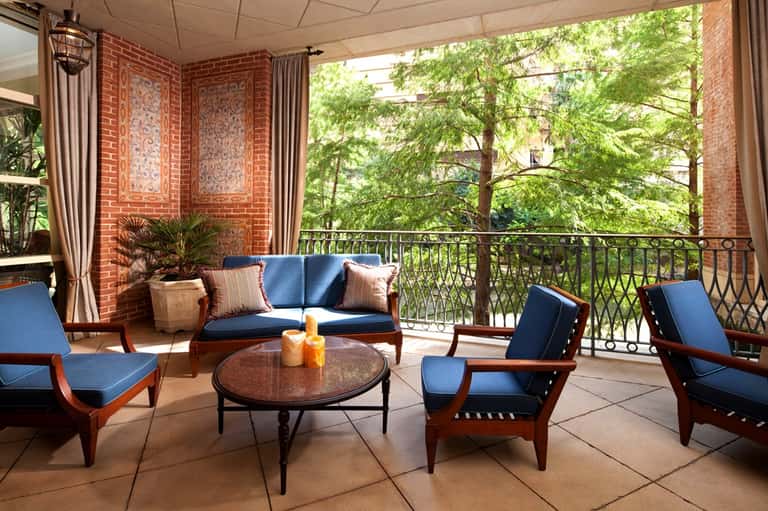 Brick terrace seating area with blue cushions, railing, and tree canopy
