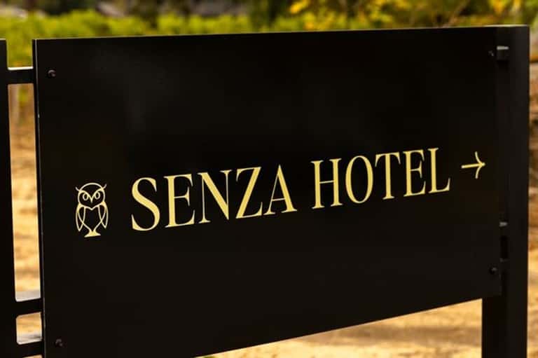 Senza Hotel directional sign with owl logo on black background nestled in nature setting
