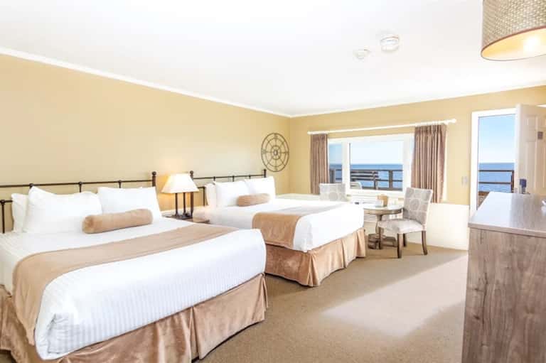 Oceanview hotel room with two beds, neutral bedding, and panoramic water views from balcony