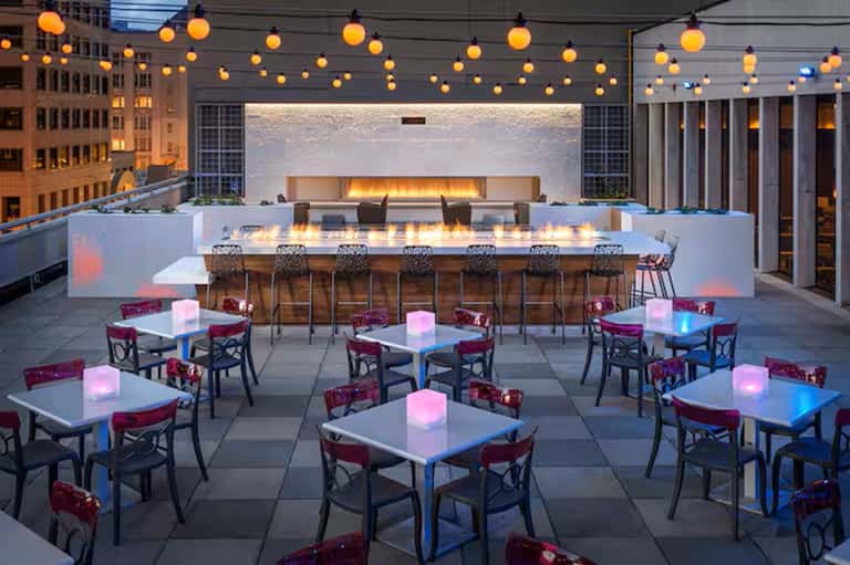 Rooftop bar and lounge with fireplace, hanging lights, glowing tables at night