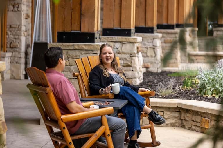 Two guests relaxing in Adirondack chairs on patio with stone fireplace