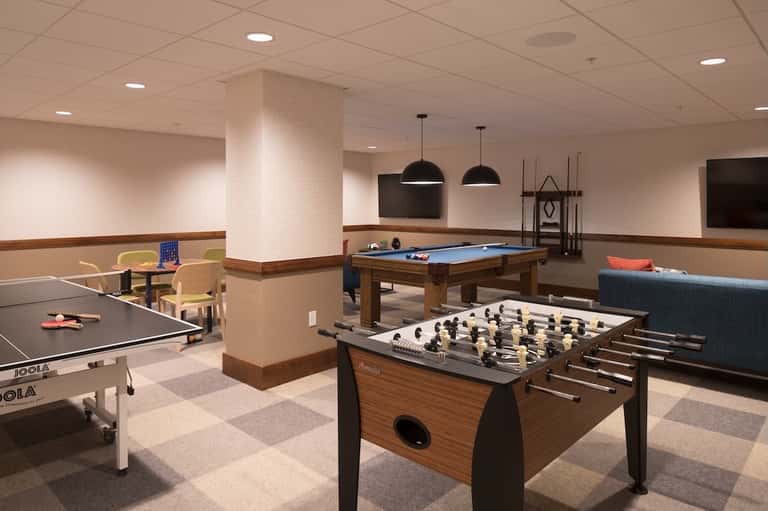 Games room with foosball table, billiards, ping pong, and lounge seating under pendant lights