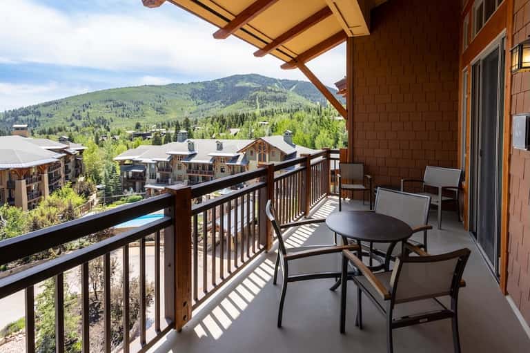 Mountain resort balcony with seating, dining table, and panoramic valley and ski slope views