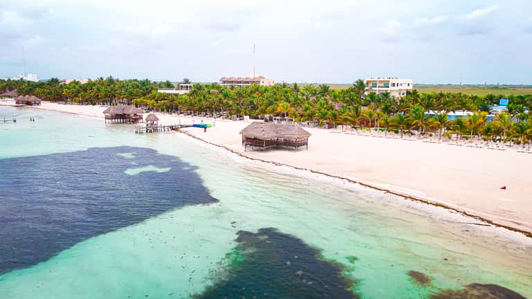 Tropical beach resort with thatched-roof structures, pristine sand, turquoise water, and palm trees