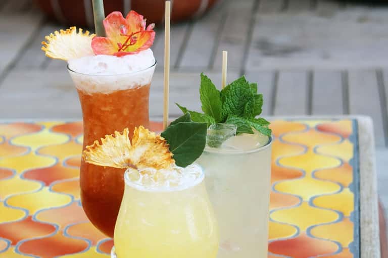 Three colorful tropical cocktails with floral garnishes on a patterned table