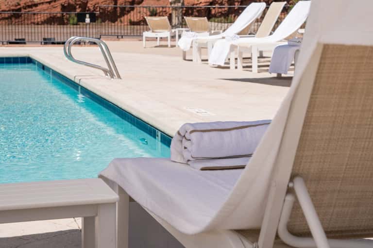 Pool deck with white lounge chairs, towels, clear turquoise water, and desert landscape backdrop
