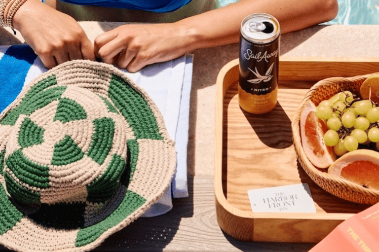 Poolside dining detail with green hat, beverage, fresh fruit, and wooden serving tray in sunlight
