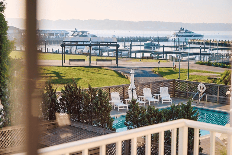 Resort waterfront deck with lounge chairs, pool, marina with boats, and scenic water views