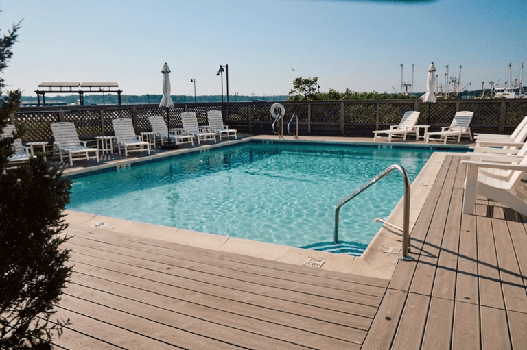 Rectangular pool with lounge chairs and umbrellas overlooking marina and boats with lattice railing