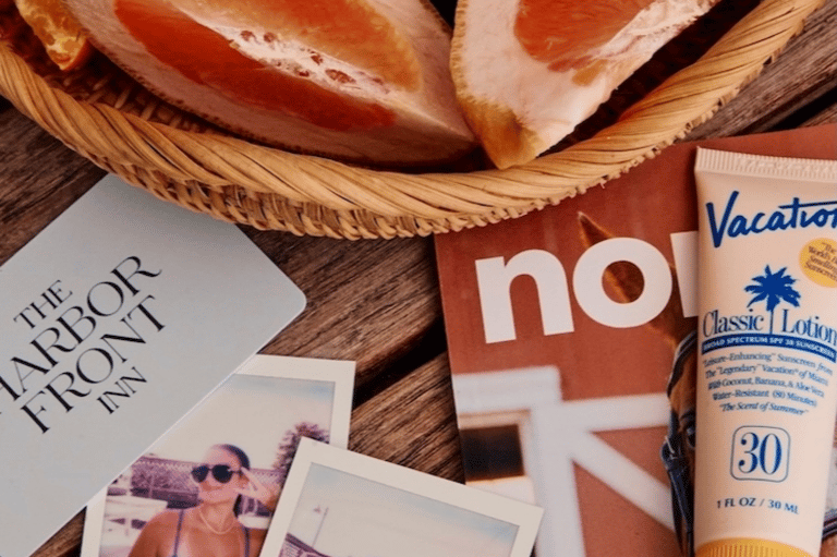Vacation flat lay with sliced prosciutto, sunscreen, magazine, and vacation brochure on wood