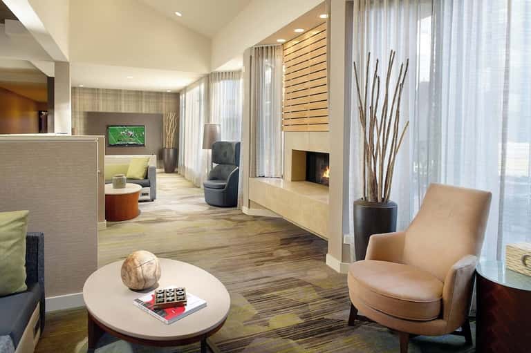 Modern hotel lounge with fireplace, comfortable seating, and floor-to-ceiling windows in neutral tones