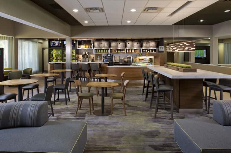 Contemporary hotel lobby and bar with wooden furniture, modern lighting, and casual seating