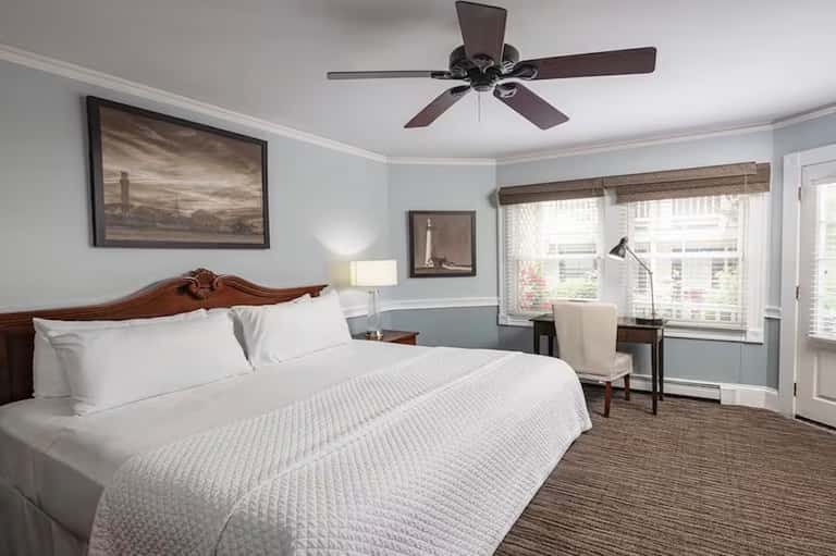 Spacious guest bedroom with queen bed, ceiling fan, framed artwork, desk area, and patio doors
