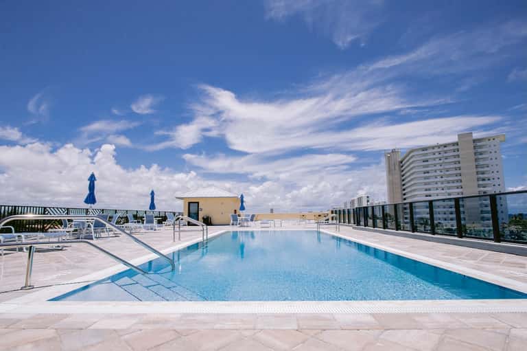Modern rooftop pool with turquoise water, white loungers, umbrellas, and city views