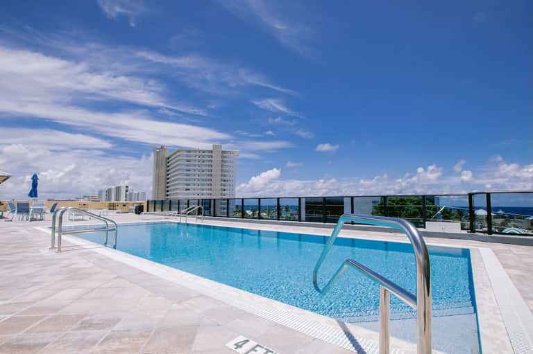 Rooftop swimming pool with metal railings, city buildings, and blue sky with clouds