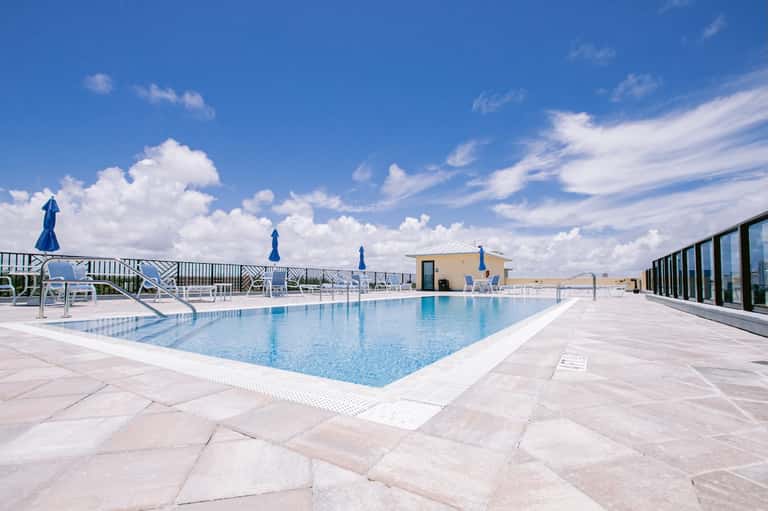 Rooftop swimming pool with blue umbrellas, white lounge chairs, and desert landscape views