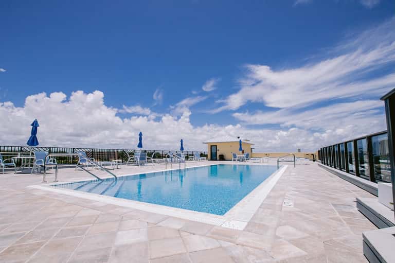 Rooftop pool overlooking the ocean with white lounge chairs, umbrellas, and modern architectural design
