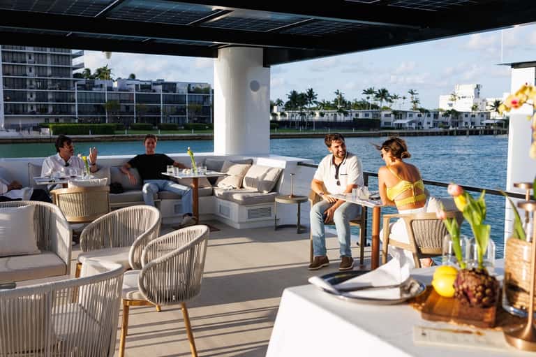 People relaxing on covered waterfront deck with modern lounge seating and water views