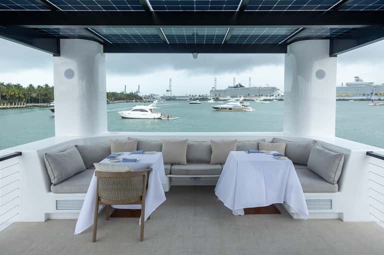 Luxury yacht dining area with gray seating, white tablecloths, and view of boats and marina