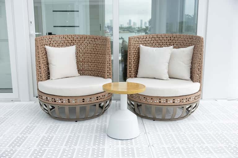 Coastal balcony with woven pod chairs, white cushions, and waterfront city skyline views