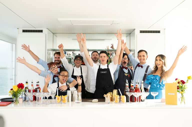 Hotel staff posing enthusiastically behind modern bar with beverages and flowers