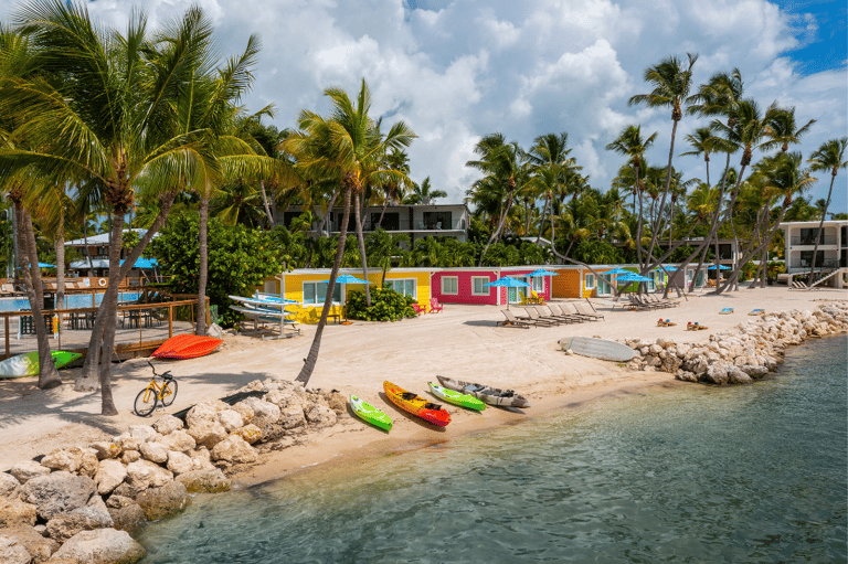 Colorful beach huts and palm trees along sandy shore with water sports equipment and resort buildings