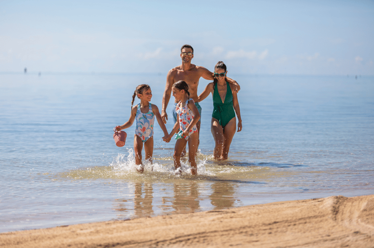 Family of four running into shallow beach water on sunny day with clear horizon