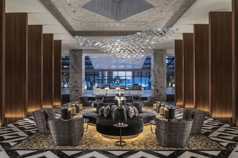 Upscale hotel lobby with chandelier, marble columns, seating areas, and floor-to-ceiling windows