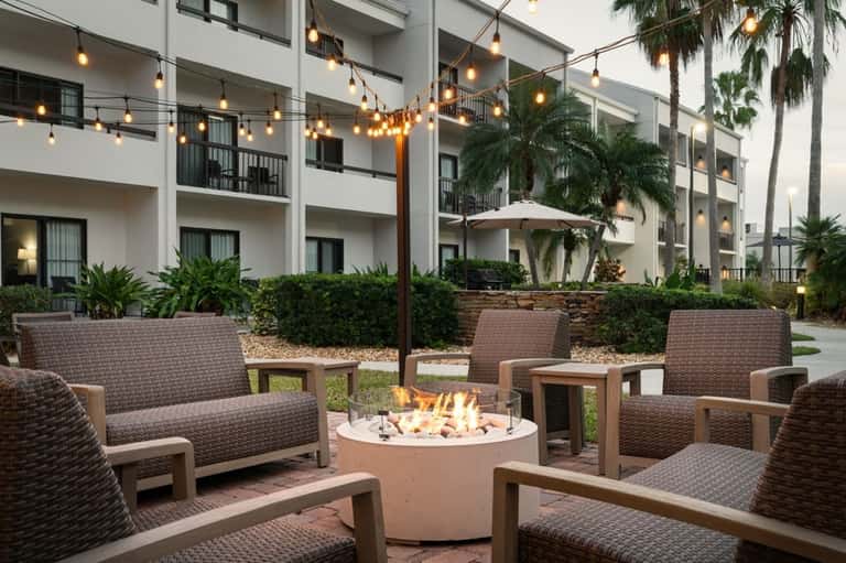 Modern hotel courtyard with fire pit, wicker seating, string lights, and white building facade