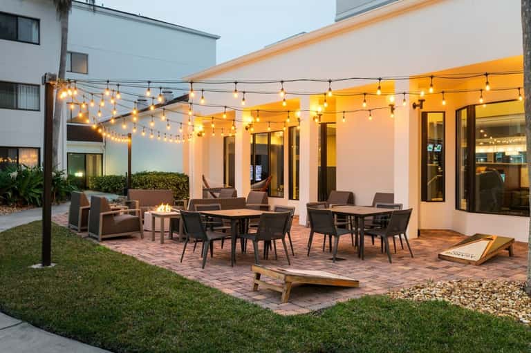 Outdoor patio with string lights, firepit, dining tables, and modern building at dusk