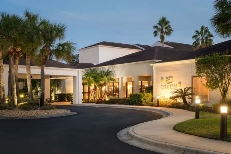 Luxury home entrance at night with palm trees, curved driveway, and landscape lighting